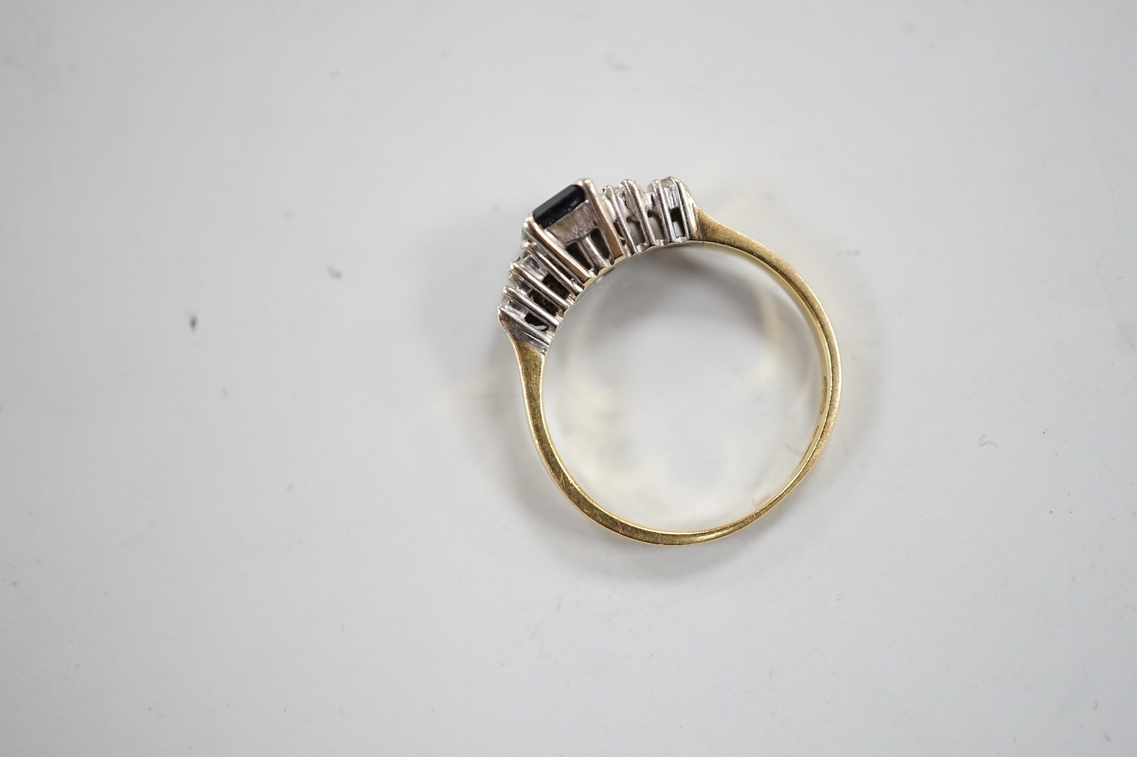 A modern 18ct gold and single stone emerald cut sapphire set ring, with graduated baguette cut diamond set shoulders, size J/K, gross weight 3.1 grams.